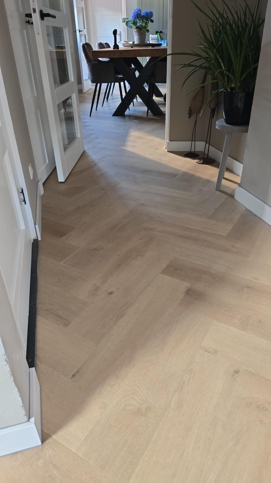 Doorkijk vanuit de hal naar de eethoek, met de visgraat doorlopend onder de deur door